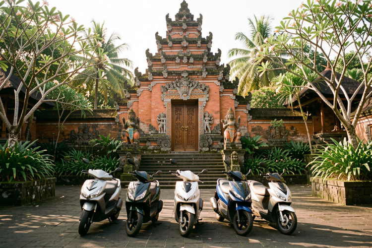 a group of modern three-wheel scooters parked in front of a Balinese temple