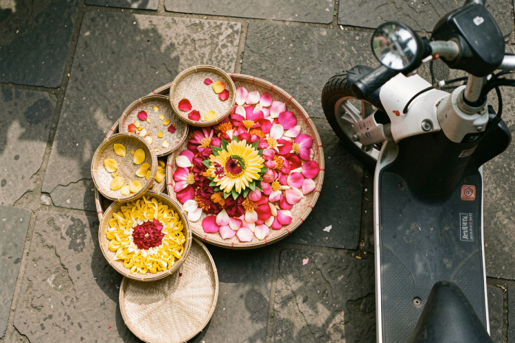 a top-down view of a 3-wheel scooter parked near a colorful Balinese flower offering on the ground